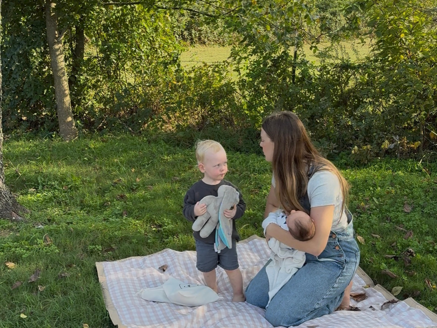 Toddler holding a soft Hoppy baby lovey while spending time outdoors with family, showing comfort and security in everyday moments.