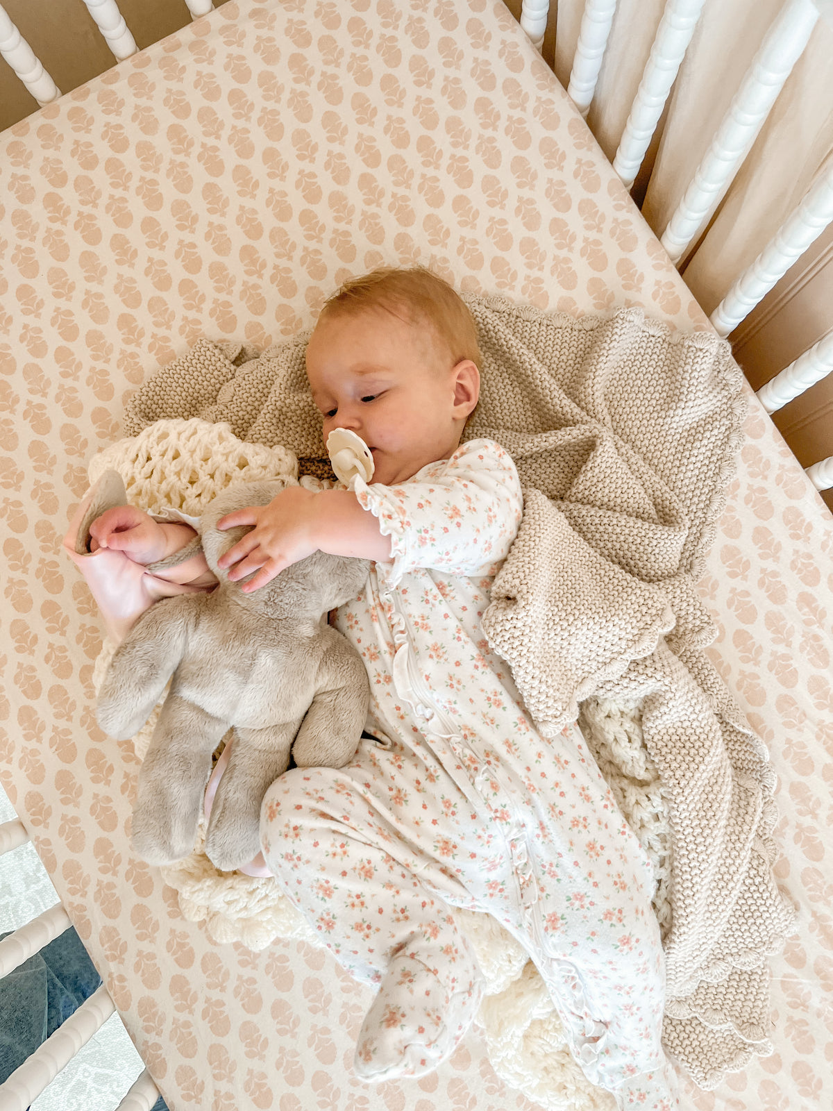 Baby lying in a crib while holding a soft Hoppy baby lovey bunny, offering comfort and soothing during quiet rest time.
